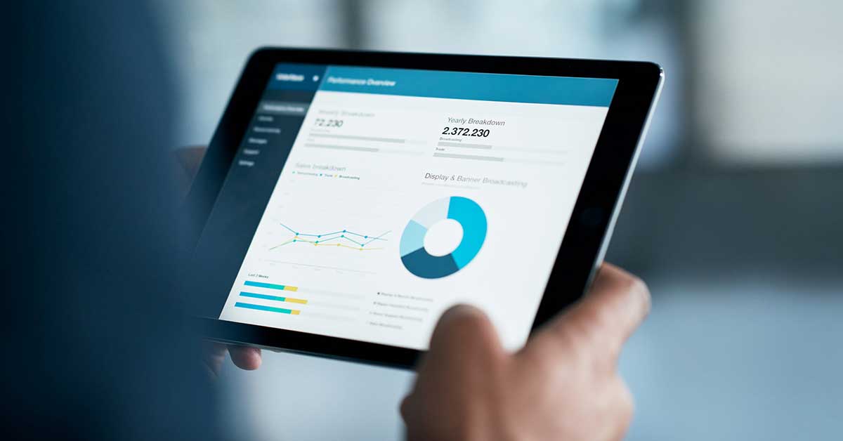Pessoa segurando um tablet com gráficos e análises de dados, ilustrando análise de dados e tendências de mercado em ambiente corporativo.