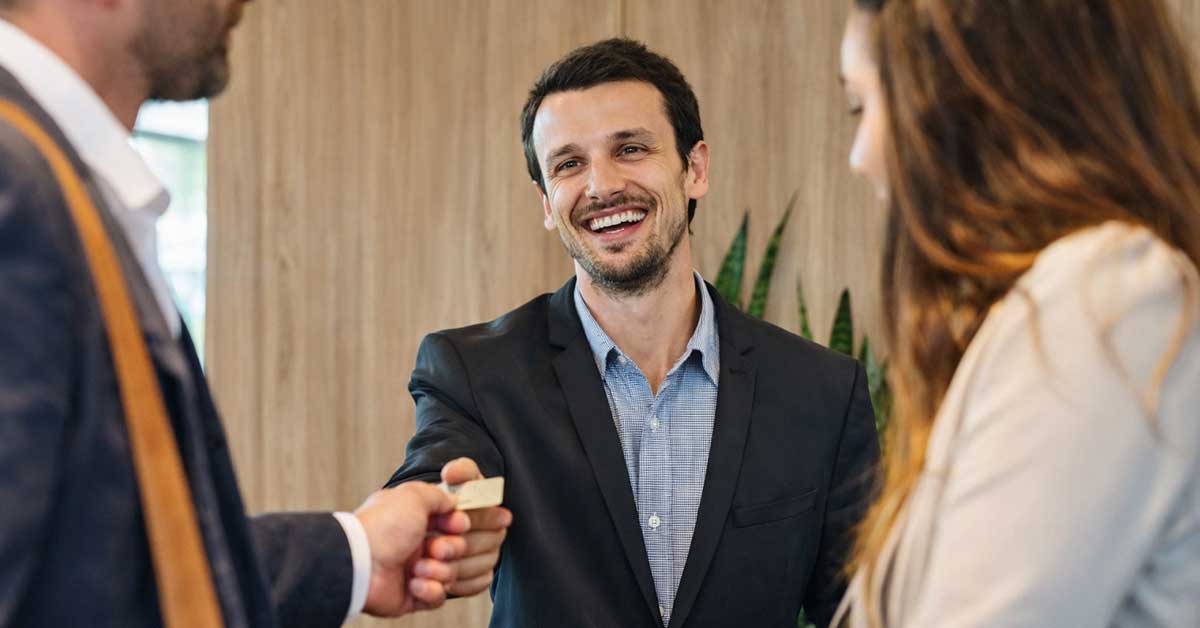 Homem de negócios sorridente fazendo networking em evento profissional, com colegas de trabalho, em ambiente moderno e acolhedor.